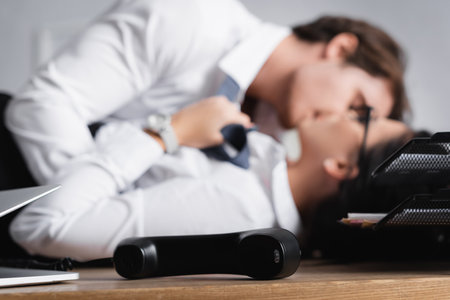selective focus of phone handset near businessman kissing secretary on blurred backgroundの写真素材
