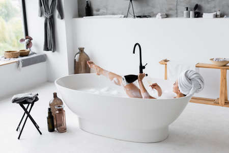 Woman with champagne taking bath in modern bathroomの写真素材