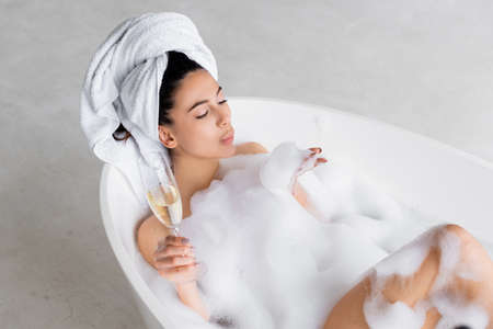 High angle view of woman blowing foam from hand while holding champagne glass in bathtubの写真素材