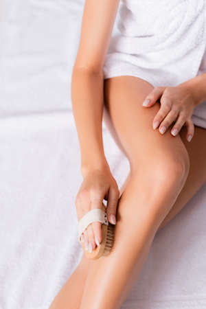 cropped view of woman wrapped in white towel exfoliating skin on legの写真素材