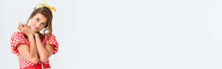 young pin up woman smiling at camera while holding hands near face isolated on whiteの写真素材