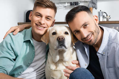 happy same sex family smiling near labrador at homeの写真素材