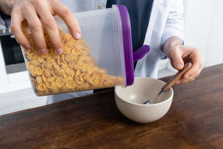 cropped view of man pouring corn flakes in bowl
