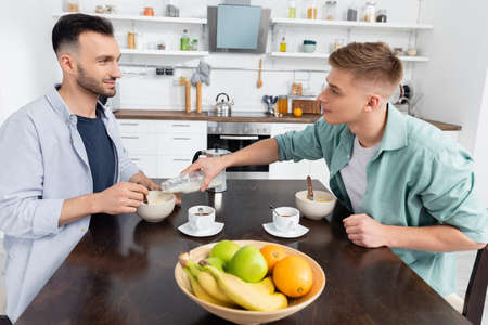 homosexual man pouring milk in bowl with corn flakes near husband