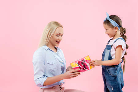 happy mother receiving greeting card from cheerful daughter isolated on pinkの写真素材
