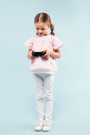 KYIV, UKRAINE - NOVEMBER 25, 2020: full length of happy kid holding joystick and standing on blue