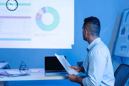 businessman holding contract near laptop with blank screen while looking at charts and graphs on...