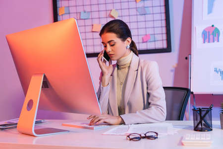 businesswoman talking on smartphone and looking at computer keyboard in officeの写真素材