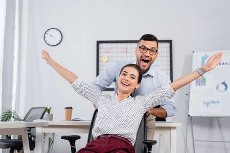excited businessman behind amazed businesswoman with outstretched hands on chairの写真素材