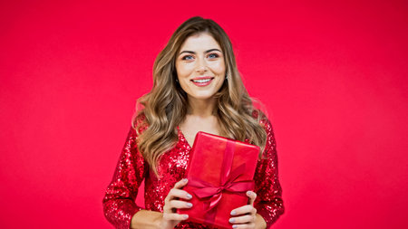 happy woman with wavy hair holding present isolated on redの写真素材