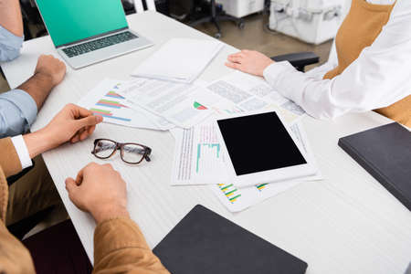 Cropped view of businesspeople sitting near devices and papers with chartsの写真素材