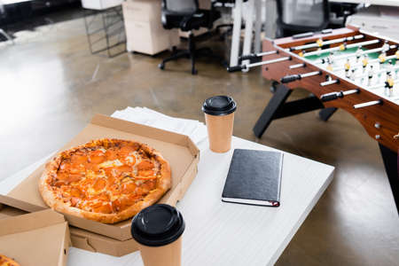 Delicious pizza, takeaway drink and notebook on office tableの写真素材