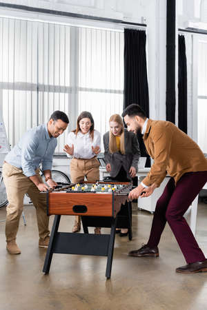 Multiethnic businessmen playing table soccer near businesswomen in officeの写真素材