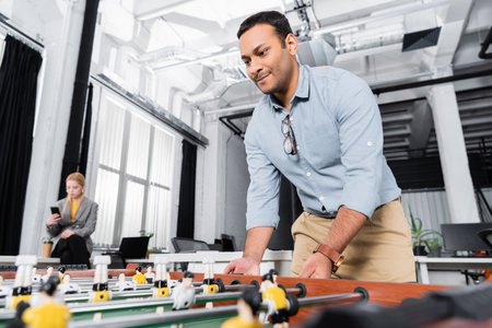 Indian businessman playing table soccer on blurred foreground in office