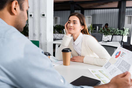 Businesswoman looking at indian colleague with papers on blurred foreground