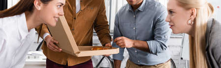 Businessmen holding pizza near businesswomen on blurred foreground in office, bannerの写真素材
