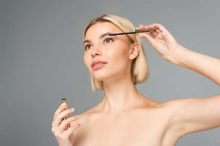 Low angle view of blonde woman holding mascara isolated on gray