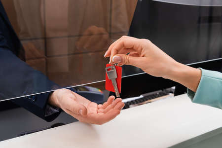 Cropped view of woman holding key near hand of manager in hotel