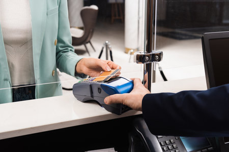Cropped view of woman paying with credit card while receptionist holding terminal in hotelの写真素材