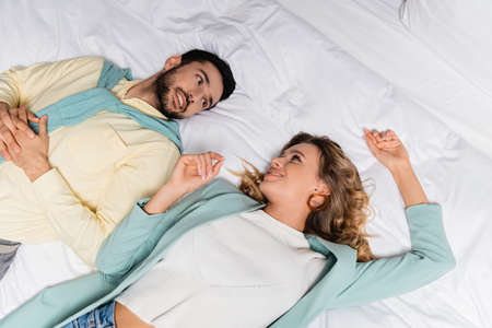 High angle view of interracial couple smiling at each other on hotel bedの写真素材