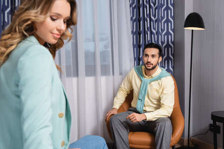 Arabian man looking at girlfriend on blurred foreground while sitting on armchair