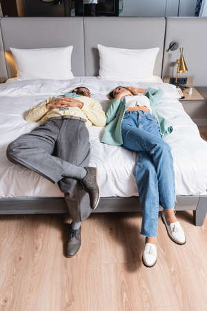 Interracial couple lying with crossed legs on hotel bedの写真素材