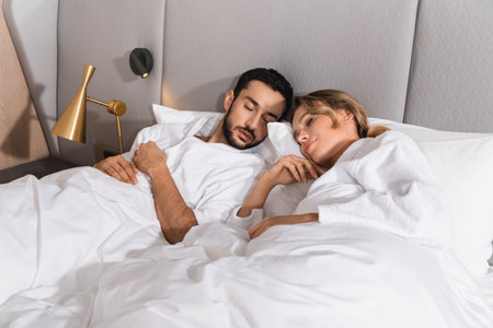 Young interracial couple sleeping on white bedding in hotelの写真素材
