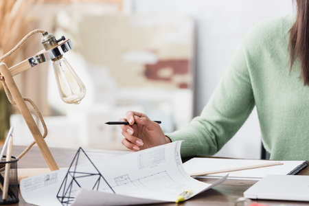cropped view of african american architect holding pencil near blueprint at workplace