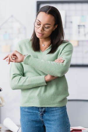 african american interior designer in eyeglasses checking time on wristwatch at homeの写真素材