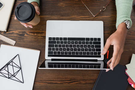 cropped view of african american architect holding coffee to go near laptop on desk