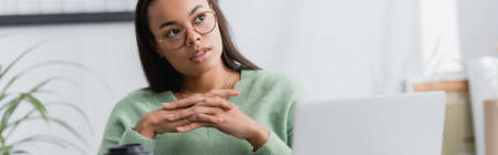 thoughtful african american freelancer looking away while sitting with clenched hands at home, bannerの写真素材