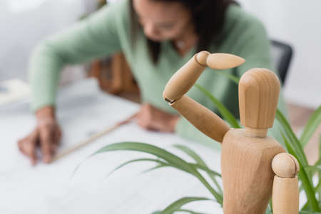 selective focus of wooden human figurine near african american architect working on blurred backgroundの写真素材