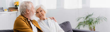 Senior couple embracing on couch at home, bannerの写真素材