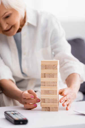 Blocks wood tower game near senior woman and remote controller on blurred foregroundの写真素材