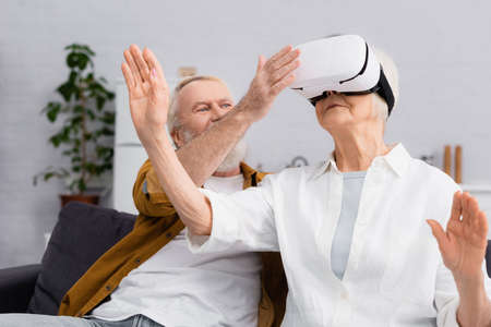 Senior man adjusting vr headset on wife at homeの写真素材