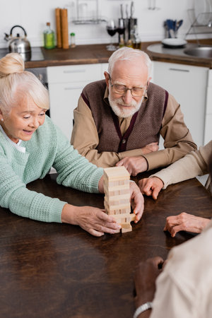 happy multicultural senior friends playing tower wood blocks game at homeの写真素材