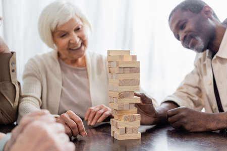 tower wood blocks on table near happy multicultural pensioners on blurred backgroundの写真素材