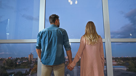 Back view of couple holding hands near window at home