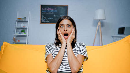 Astonished woman sitting on yellow sofa at homeの写真素材