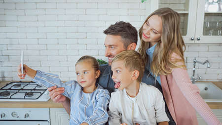 Cheerful family taking selfie with smartphone in kitchenの写真素材
