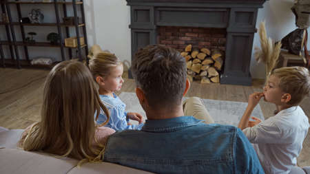 Children sitting near parents on blurred foreground on couch in living roomの写真素材
