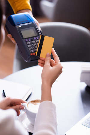 partial view of woman holding credit card near credit card reader in hand of waiterの写真素材