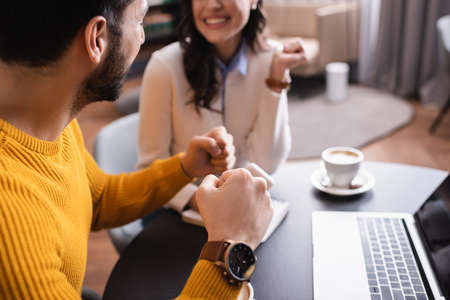 Arabian man showing yeah gesture near laptop and friend on blurred background in restaurantの写真素材