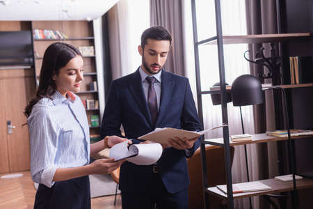 Young businesswoman holding clipboard near arabian partner in modern restaurant