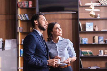 happy interracial business partners looking away while holding cups of coffee in restaurantの写真素材
