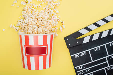 top view of bucket with tasty popcorn near clapperboard on yellow, cinema conceptの写真素材