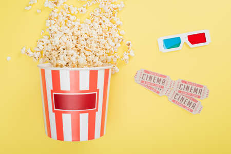 top view of bucket with popcorn, 3d glasses and cinema tickets on yellowの写真素材