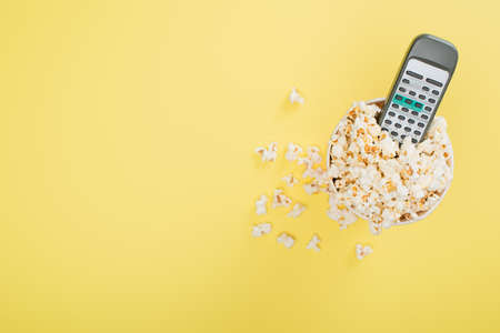 top view of tv remote controller in bucket full of popcorn on yellow, cinema conceptの写真素材