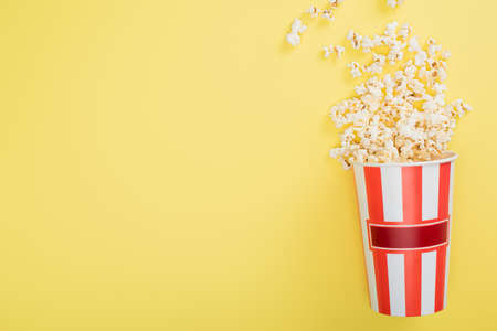 top view of striped bucket with crunchy popcorn on yellow, cinema conceptの写真素材