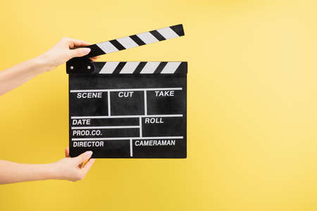 partial view of camera assistant holding clapperboard isolated on yellow, cinema conceptの写真素材